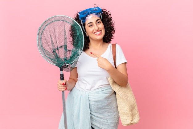 Mulher bonita árabe sorrindo alegremente, sentindo-se feliz e apontando para o lado com óculos de proteção. conceito de pescador