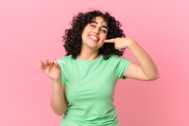 Mulher bonita árabe sorrindo com confiança, apontando para o próprio sorriso largo. conceito de não fumar