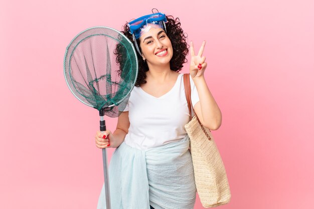 Mulher bonita árabe sorrindo e parecendo amigável, mostrando o número dois com óculos de proteção. conceito de pescador