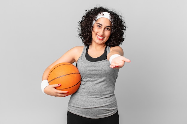 Mulher bonita árabe sorrindo feliz com amigável e oferecendo e mostrando um conceito e segurando uma bola de basquete. conceito de esporte