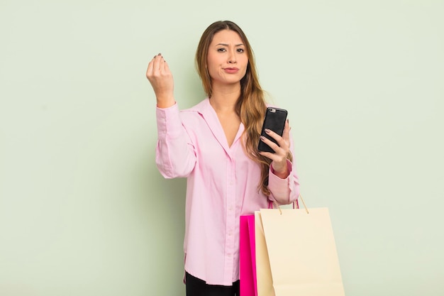 Mulher bonita asiática fazendo gesto de capice ou dinheiro, dizendo para você pagar. conceito de sacolas de compras