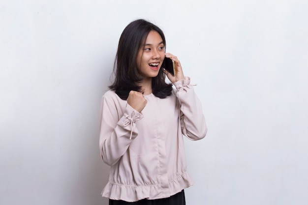 Mulher bonita asiática jovem feliz usando telefone celular isolado no fundo branco