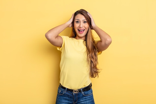 Mulher bonita asiática levantando as mãos na cabeça, de boca aberta, sentindo-se extremamente sortuda, surpresa, animada e feliz