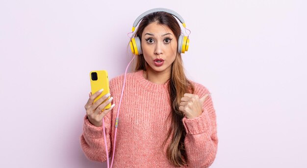 Mulher bonita asiática parecendo espantada com a descrença. fones de ouvido e conceito de telefone