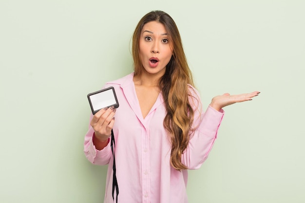 Mulher bonita asiática parecendo surpresa e chocada com o queixo caído segurando um conceito de identificação de cartão de passagem de objeto