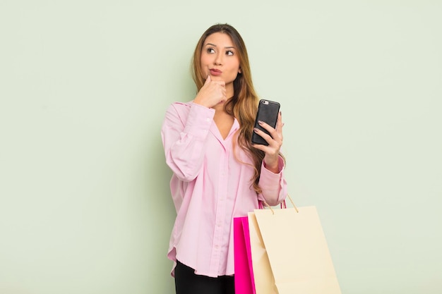 Mulher bonita asiática pensando, sentindo-se duvidosa e confusa. conceito de sacolas de compras