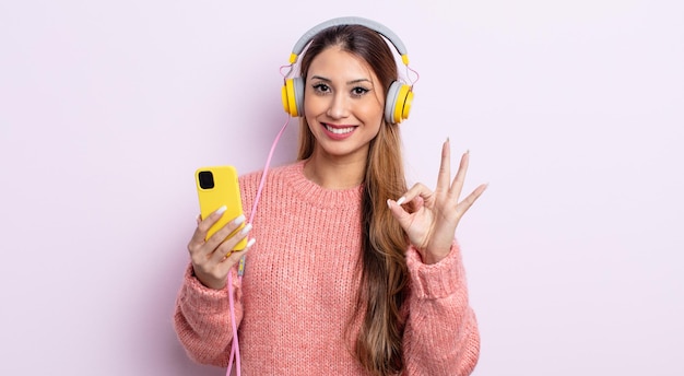 Mulher bonita asiática se sentindo feliz, mostrando aprovação com gesto bem. fones de ouvido e conceito de telefone