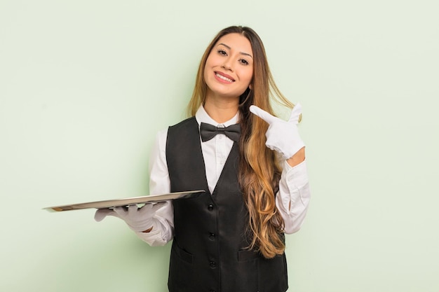 Mulher bonita asiática sorrindo com confiança apontando para o próprio garçom de sorriso largo e conceito de bandeja