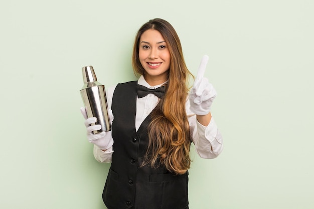 Mulher bonita asiática sorrindo e parecendo amigável, mostrando o número um. barman com um shaker