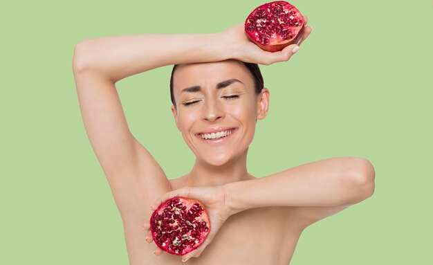 Mulher bonita brilhante e emocional com meia romã nas mãos posando na frente da câmera Fruta é saúde