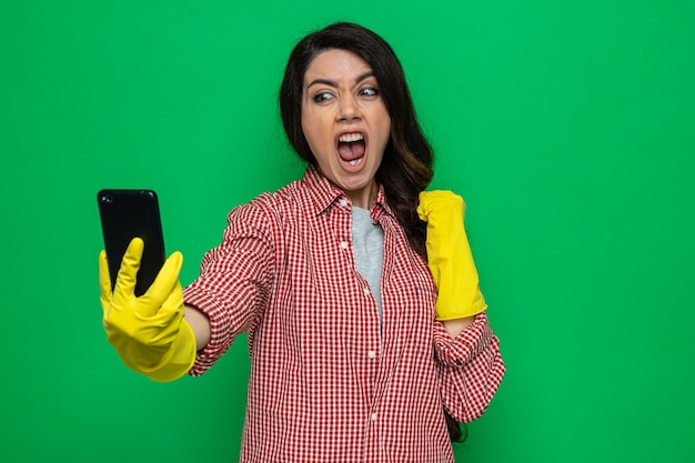 Mulher bonita caucasiana de limpeza irritada com luvas de borracha segurando e segurando o punho