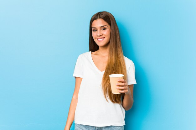 Mulher bonita caucasiana jovem segurando um café para viagem feliz, sorridente e alegre.