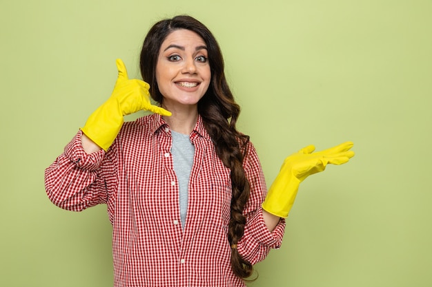 Mulher bonita caucasiana limpadora sorridente com luvas de borracha, mantendo a mão aberta e gesticulando para ligar para mim