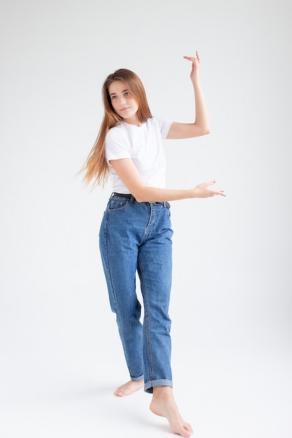 Mulher bonita caucasiana magra dançando no fundo branco do estúdio com os pés descalços