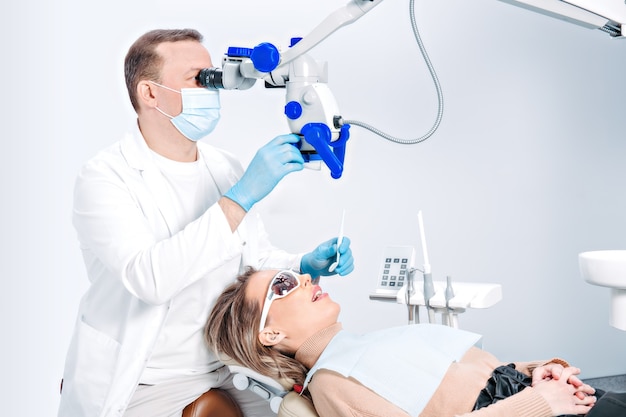 Mulher bonita caucasiana na cadeira do dentista na clínica odontológica moderna. médico check-up do paciente usando equipamento profissional odontológico, microscópio. paciente do sexo feminino em atendimento odontológico.