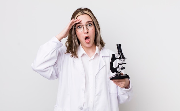 Mulher bonita caucasiana olhando feliz cientista surpreso e surpreso com o conceito de microscópio