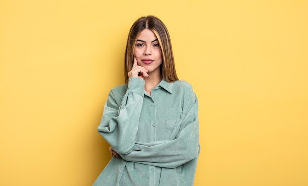 mulher bonita caucasiana olhando feliz e sorrindo com a mão no queixo, imaginando ou fazendo uma pergunta, comparando opções