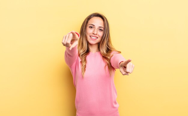 Mulher bonita caucasiana se sentindo feliz e confiante, apontando para a câmera com as duas mãos e rindo, escolhendo você