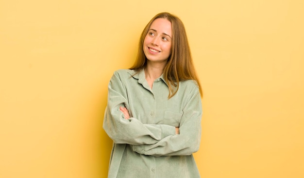 Mulher bonita caucasiana se sentindo feliz, orgulhosa e esperançosa pensando ou pensando olhando para cima para copiar o espaço com braços cruzados