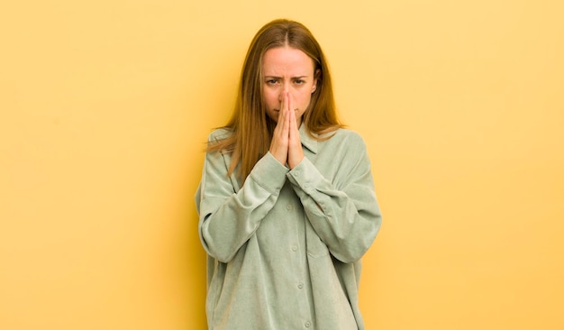 Mulher bonita caucasiana se sentindo preocupada, esperançosa e religiosa rezando fielmente com as palmas das mãos pressionadas implorando perdão