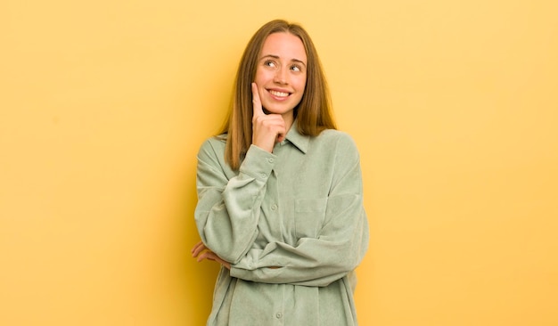 Mulher bonita caucasiana sorrindo alegremente e sonhando acordado ou duvidando de olhar para o lado