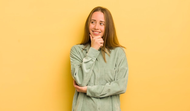 Mulher bonita caucasiana sorrindo com uma expressão feliz e confiante com a mão no queixo pensando e olhando para o lado