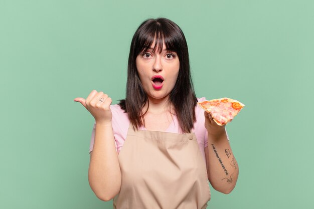 Mulher bonita chef com expressão de medo e segurando uma pizza