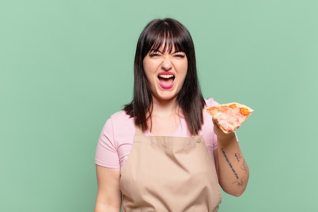Mulher bonita chef com expressão de raiva e segurando uma pizza