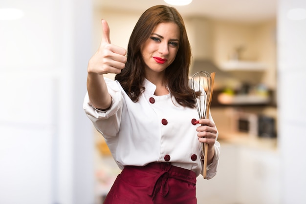 Mulher bonita chef com o polegar para cima em fundo desfocado