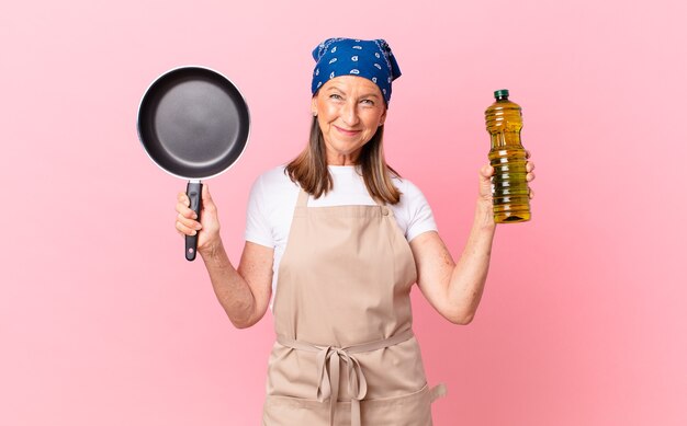 Mulher bonita chef de meia-idade segurando uma panela e uma garrafa de azeite