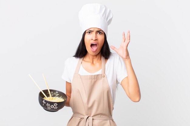 Mulher bonita chef hispânica gritando com as mãos para o alto e segurando uma tigela de macarrão