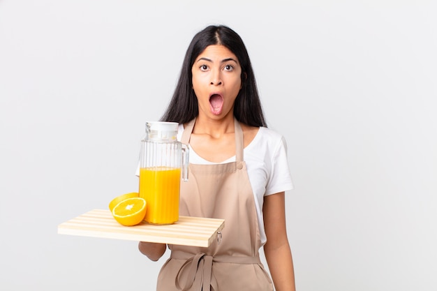 Mulher bonita, chef hispânica, muito chocada ou surpresa, segurando um suco de laranja