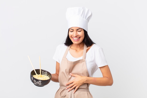 Mulher bonita, chef hispânica, rindo alto de uma piada hilária e segurando uma tigela de macarrão