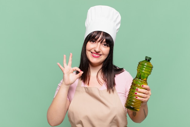 Mulher bonita chefe com uma expressão feliz e segurando uma garrafa de azeite