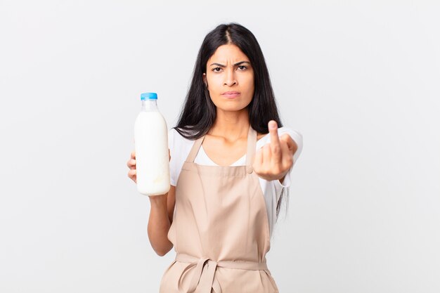 Mulher bonita chefe hispânica se sentindo irritada, irritada, rebelde e agressiva e segurando uma garrafa de leite