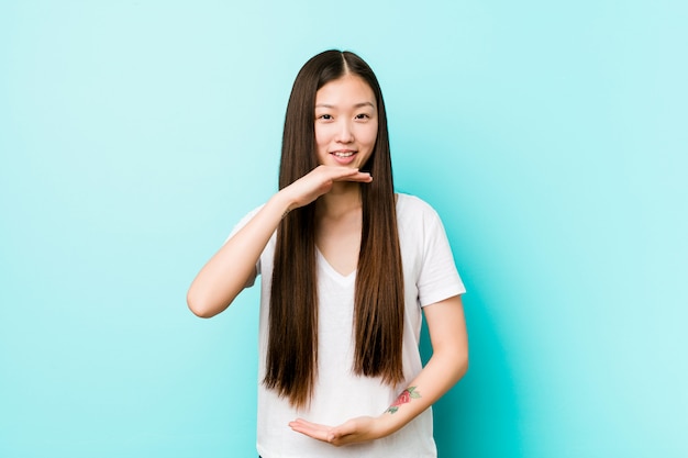 Mulher bonita chinesa jovem segurando algo com ambas as mãos, apresentação do produto.