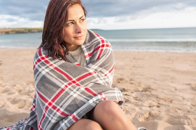 Mulher bonita coberta com cobertor na praia