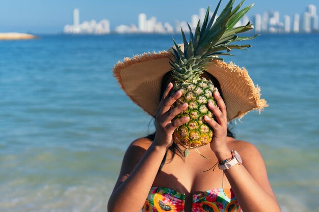 Mulher bonita com abacaxi no rosto caminhando na praia