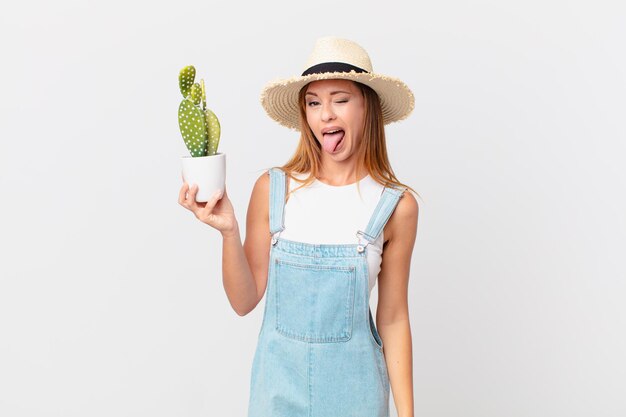 Mulher bonita com atitude alegre e rebelde brincando e enfiando a língua para fora e segurando uma planta decorativa de cacto