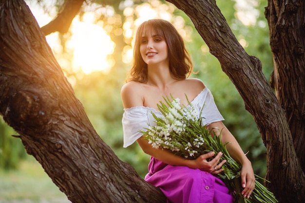 Mulher bonita com buquê de flores silvestres no pôr do sol ilumina o horário de verão