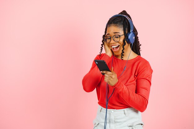 Mulher bonita com cabelo afro ouvindo música e dançando no fundo rosa