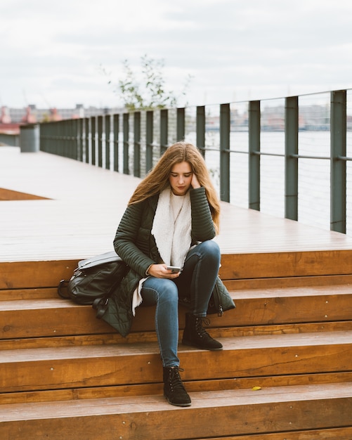 Mulher bonita com cabelo comprido senta-se nas escadas com telefone em seu han