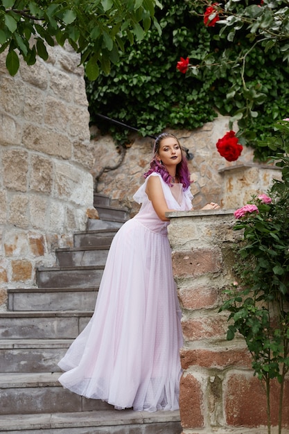 Mulher bonita com cabelo roxo em um vestido de noiva branco caminha no jardim. Maquiagem natural