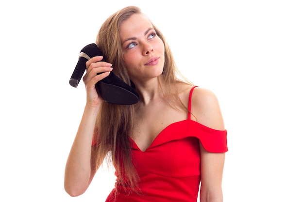 Mulher bonita com cabelos castanhos compridos em vestido vermelho acanhado segurando um par de sapatos de estilete preto