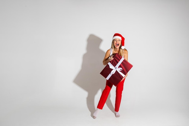 Mulher bonita com chapéu de Natal vermelho e branco segurando uma caixa grande com um presente e se alegra