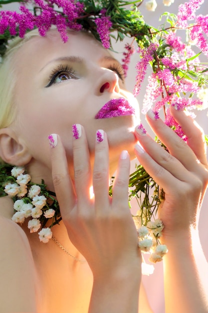 Mulher bonita com desenho de flor rosa de verão Astilbe nos lábios e nos dedos