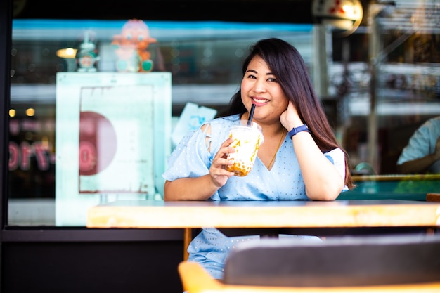 Mulher bonita com excesso de peso em uma cafeteria, Mulher asiática feliz em uma cafeteria com um copo de plástico de café