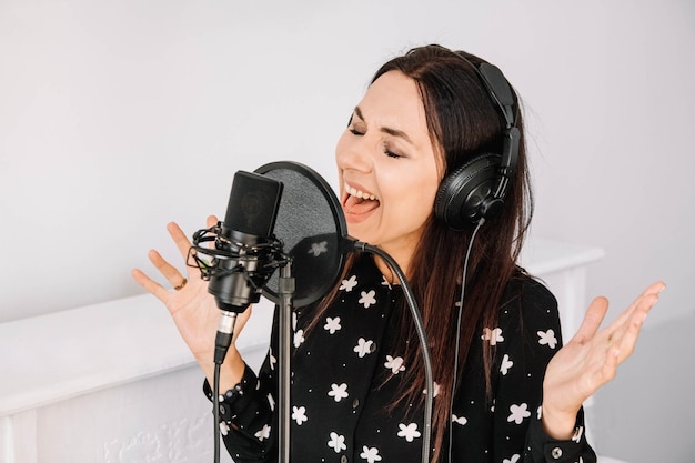 Mulher bonita com fones de ouvido canta uma música perto de um microfone em um estúdio de gravação
