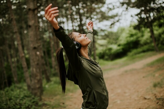 Mulher bonita com fones de ouvido espetados nos braços na floresta porque gosta de treinar ao ar livre