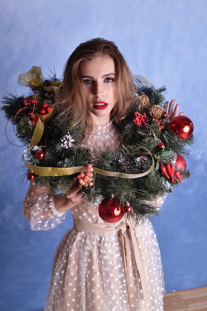 Mulher bonita com guirlanda de Natal nas mãos sobre fundo azul